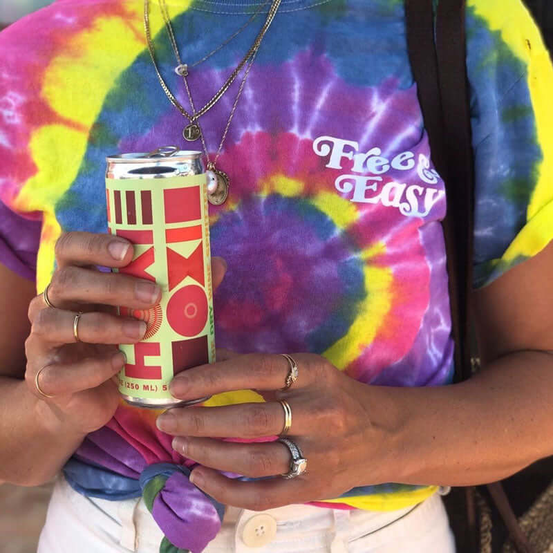 A woman holding a can of HOXIE Wine Spritzer wearing a tie dye shirt