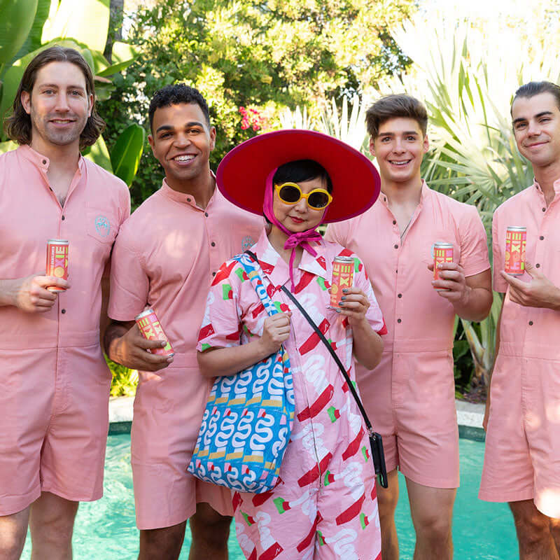 A group of people smiling wearing pink clothing holding cans of HOXIE Wine Spritzer 